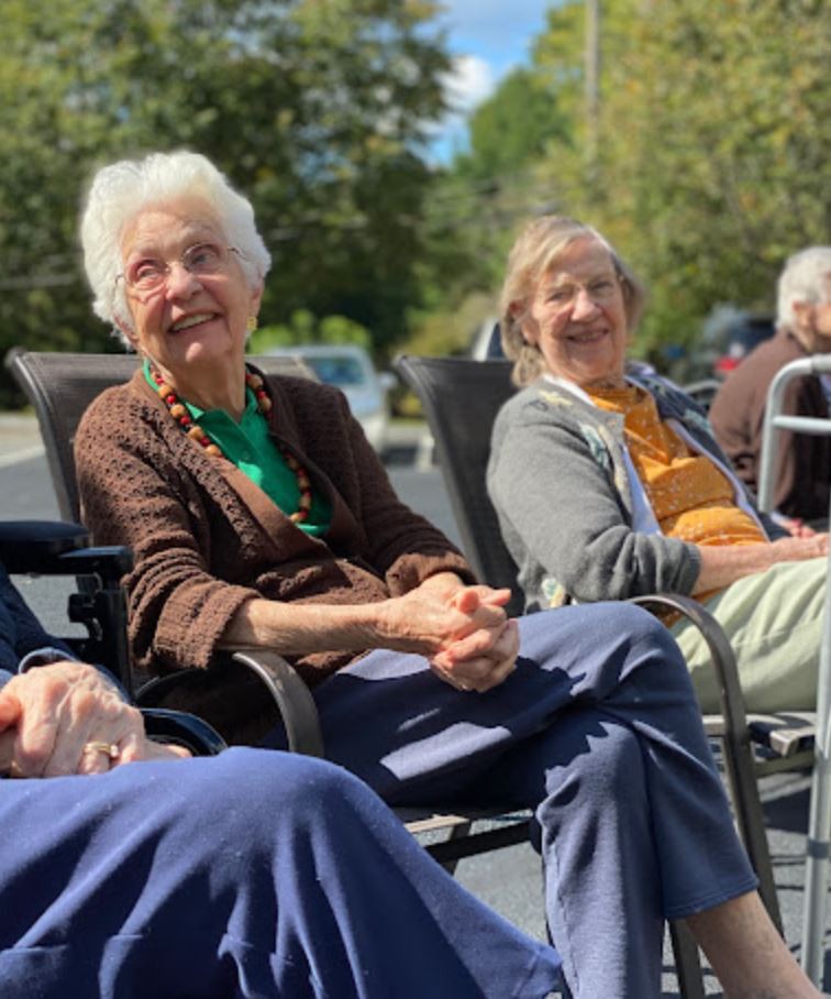 A group of elderly individuals enjoying a sunny day outdoors, sitting and smiling on chairs.