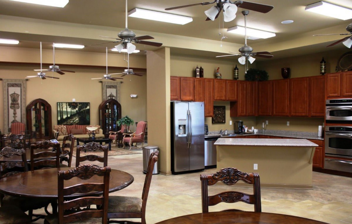 An open kitchen and dining area with wooden cabinetry, stainless steel appliances, ceiling fans, and decorative indoor plants.