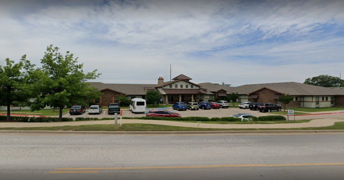A view of a large building with a parking lot and several cars parked, seen from across the road.