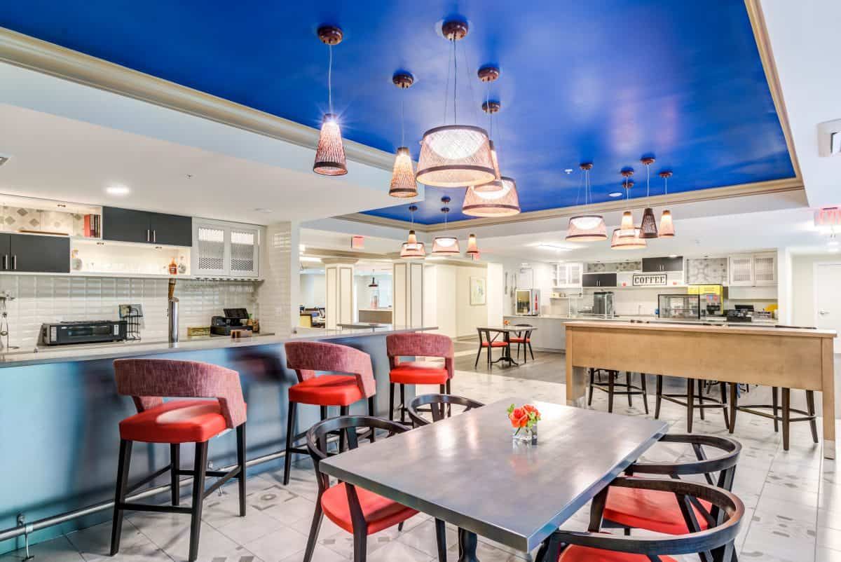 A modern restaurant interior with vibrant lighting, red cushioned chairs, and a striking blue ceiling.