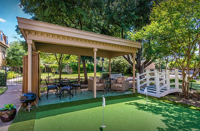 A charming backyard with a gazebo and putting green surrounded by lush trees.