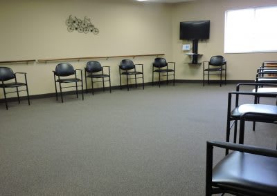 An empty waiting room with chairs arranged along the walls and a television mounted on the corner.