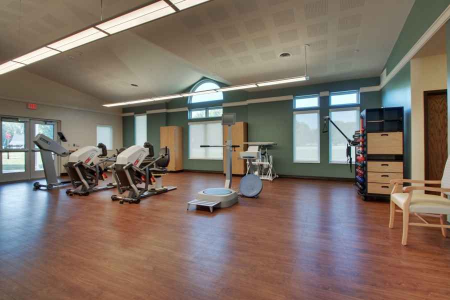 A spacious gym with modern exercise equipment and wooden flooring.