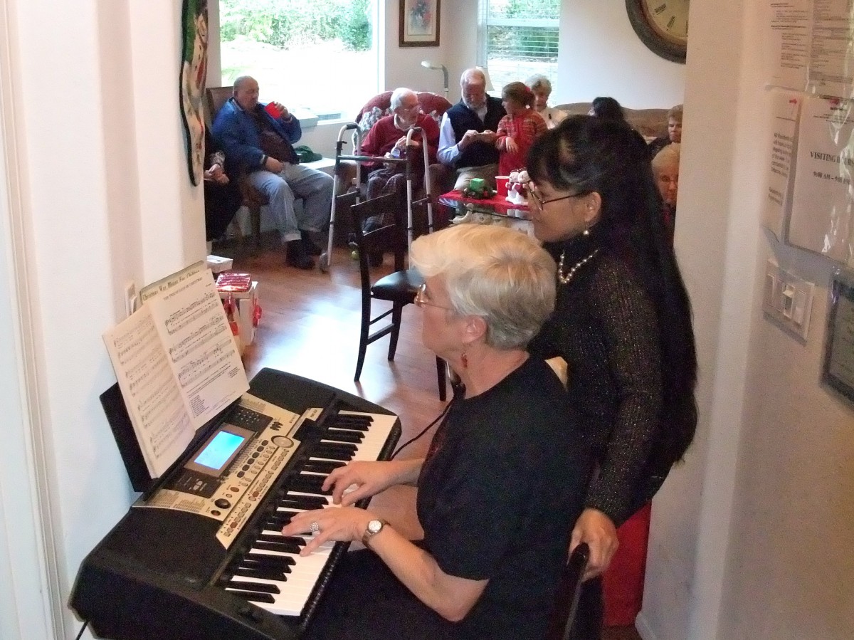 Two people performing music on a keyboard for an audience indoors.