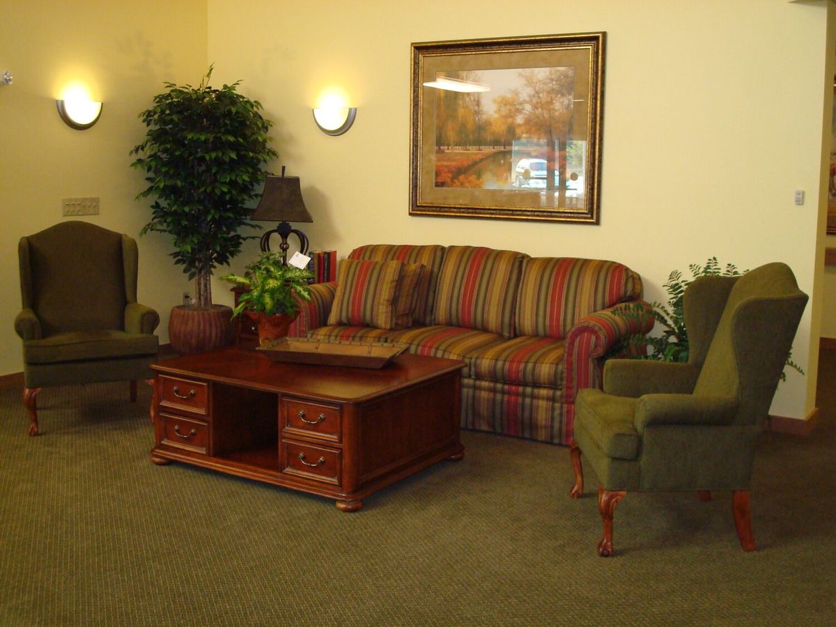 A cozy living room with striped sofa, two armchairs, a wooden coffee table, and framed artwork on the wall.