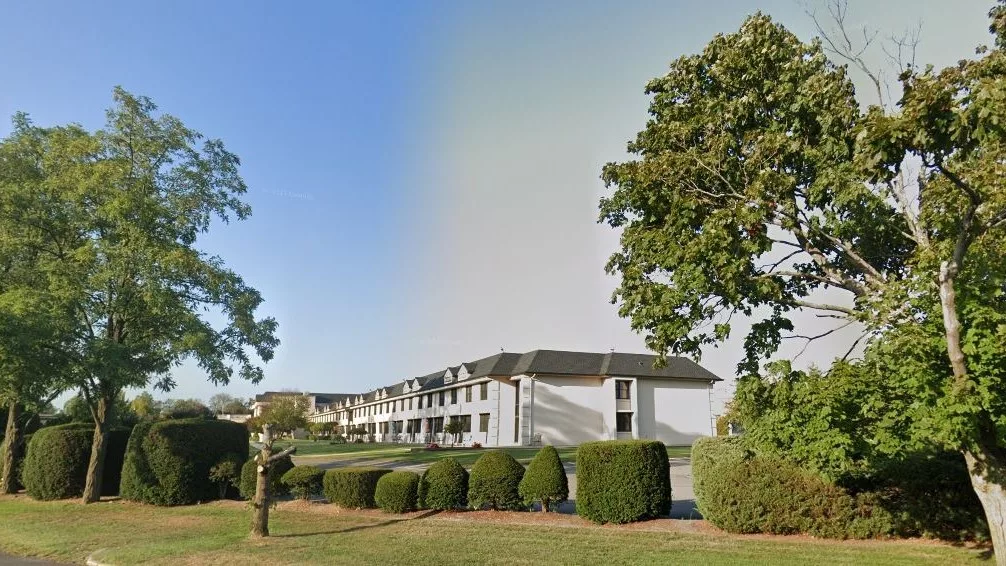 A white building surrounded by trees and bushes under a clear sky.