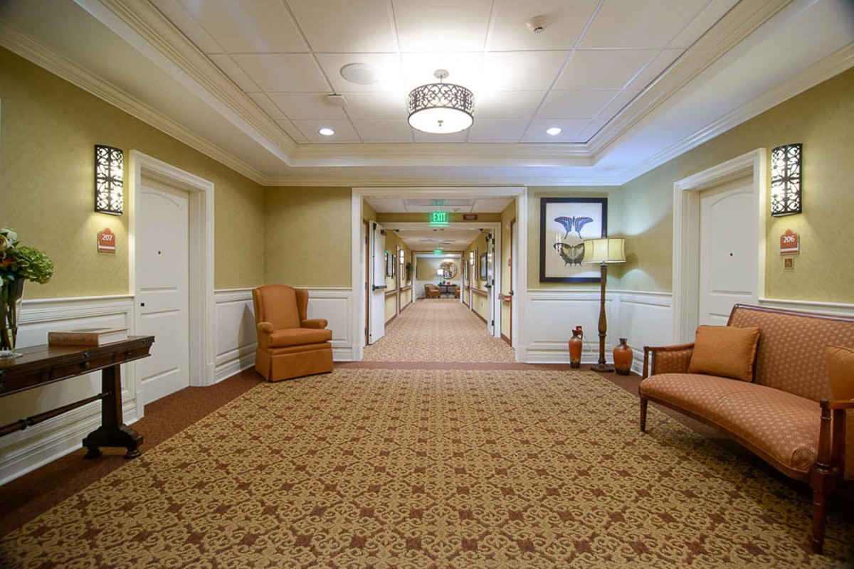 A well-lit hallway with carpet and seating area, resembling a hotel interior.