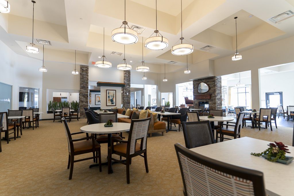 A spacious and modern lounge area with tables and chairs, featuring elegant lighting fixtures.