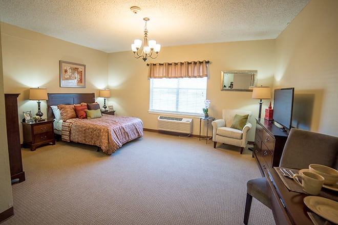 A spacious and well-lit bedroom with a bed, armchair, and decorative elements.