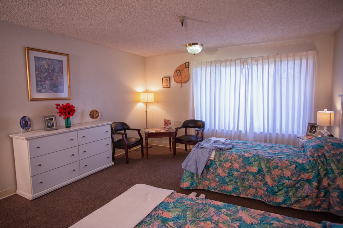 A cozy bedroom with twin beds, floral bedding, and a warm lamp by the window.