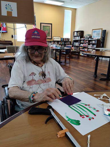 An elderly woman engages in a creative crafting activity at a senior center, using colorful materials.