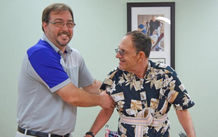 Two men are smiling and interacting in a casual indoor setting.