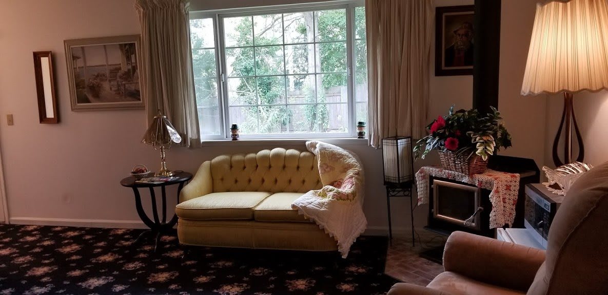 A cozy living room featuring a yellow sofa by the window, complemented by curtains and a decorative lamp.