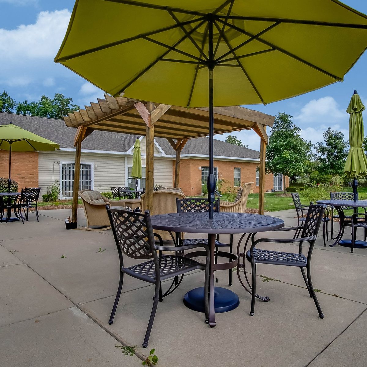 A sunny day on a patio with tables, chairs, and umbrellas next to a brick building.