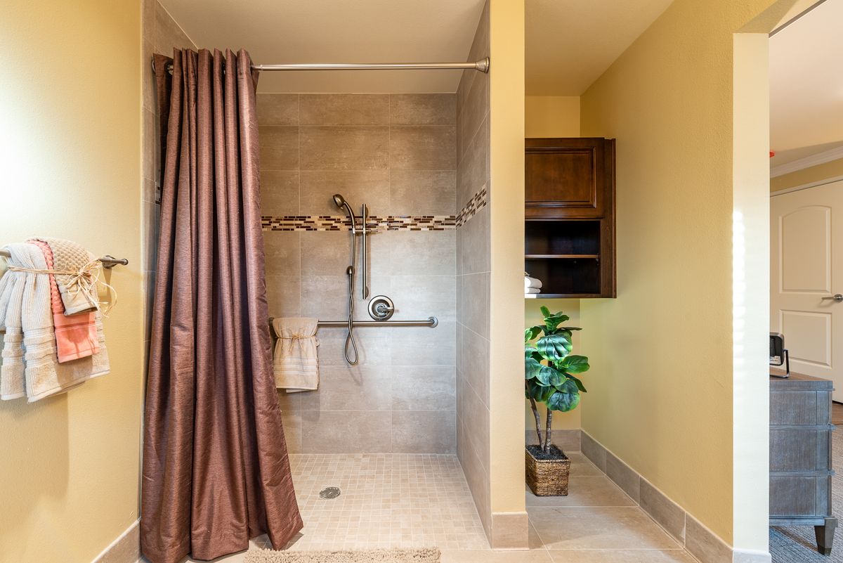 A modern bathroom with a walk-in shower, brown curtain, and indoor plant.