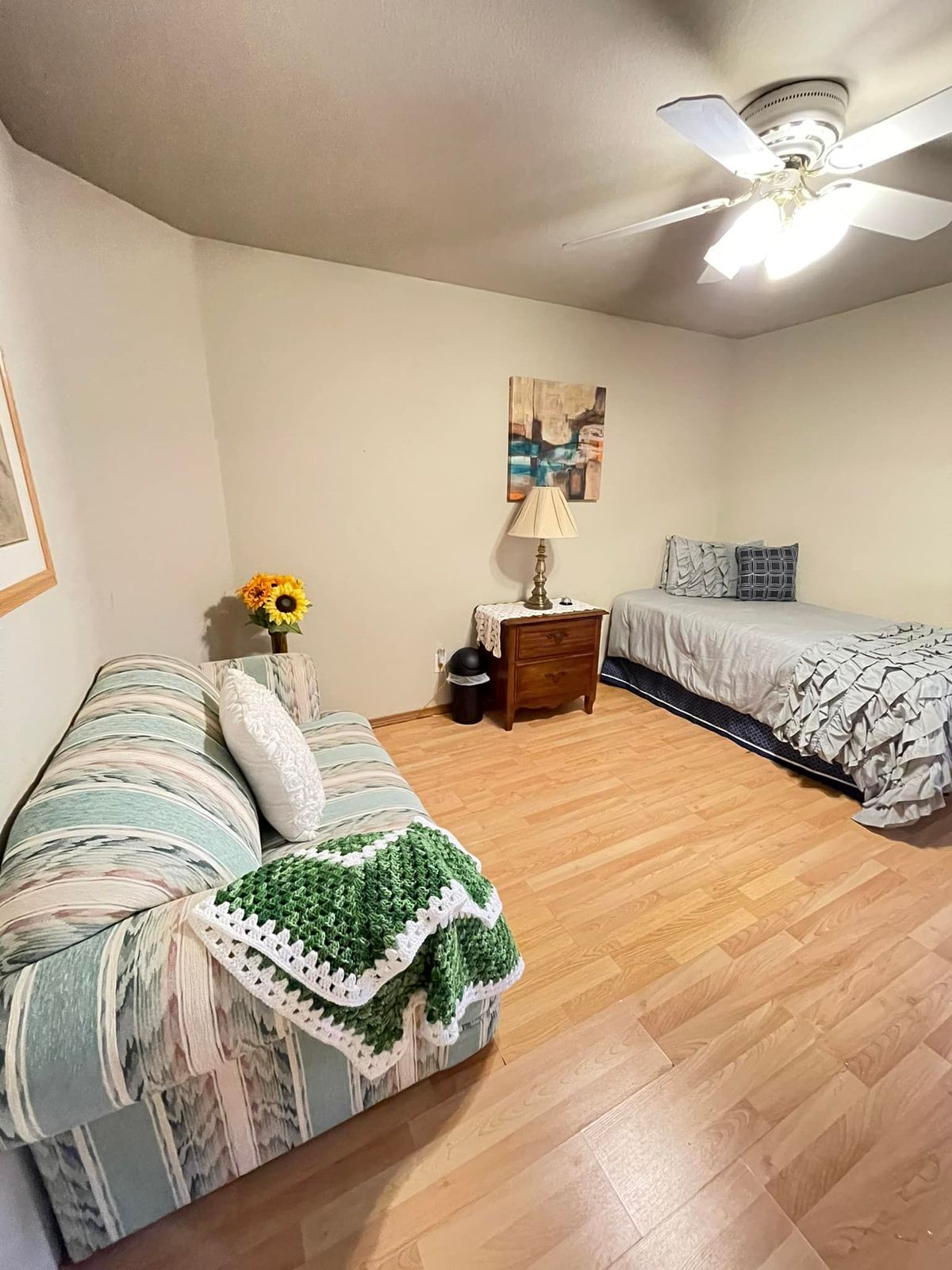 A cozy bedroom with a single bed and sofa, featuring wooden flooring and simple decor.