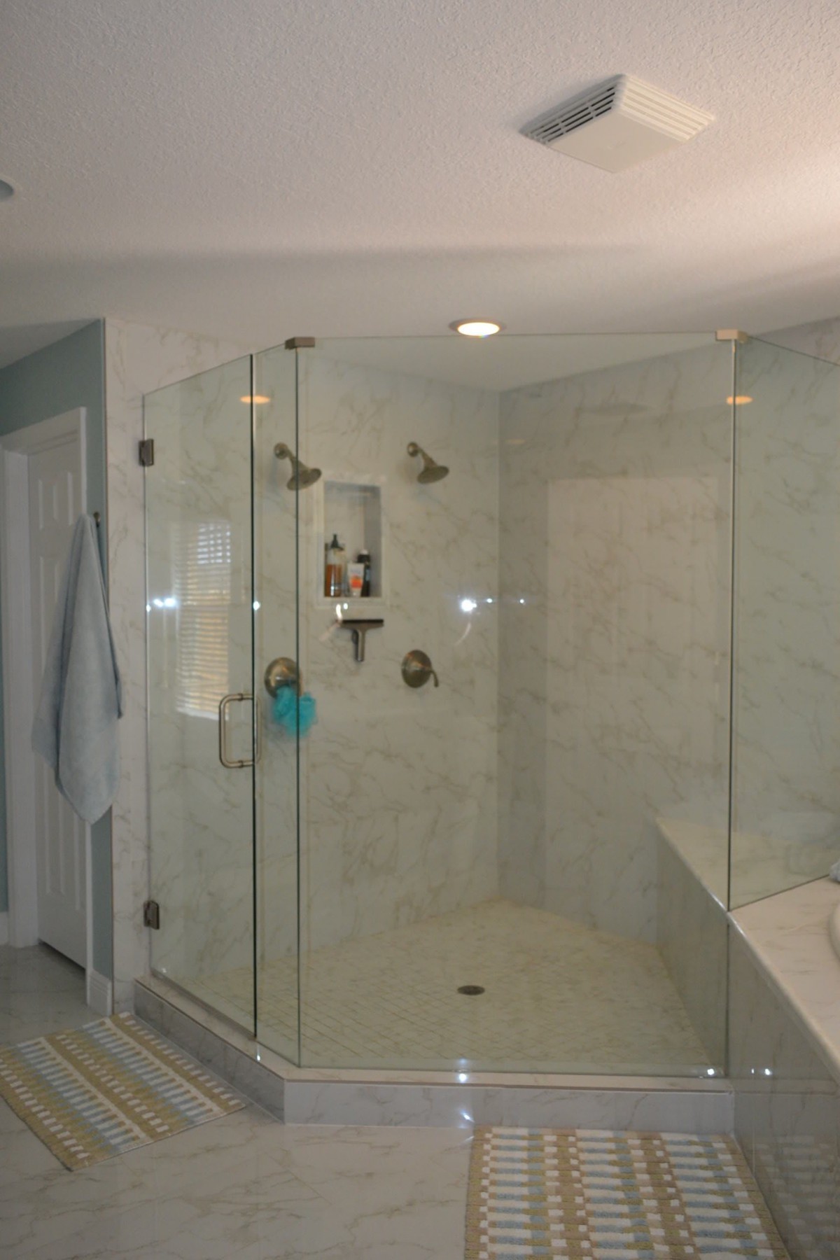 A modern bathroom with a glass-enclosed shower and marble tile walls.