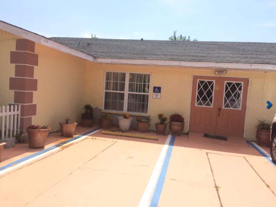 A small house with a driveway, windows, doors, and potted plants.