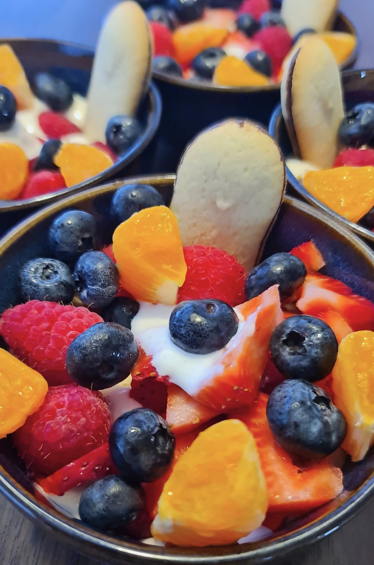 A colorful fruit salad with blueberries, raspberries, strawberries, oranges, yogurt, and a cookie garnish.
