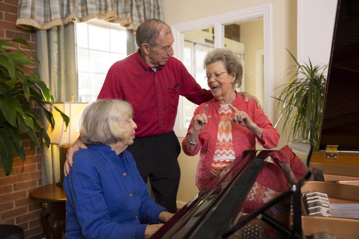 A group of seniors enjoying a musical moment around the piano indoors.