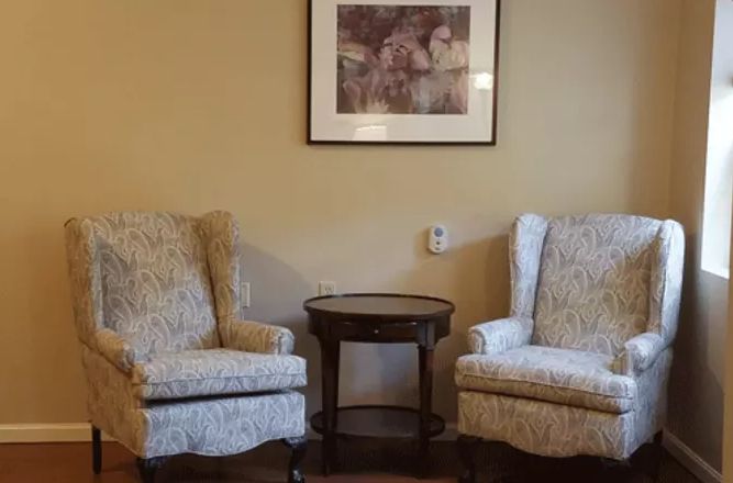 A cozy seating area with two upholstered chairs flanking a small round table, complemented by a framed artwork on the wall.