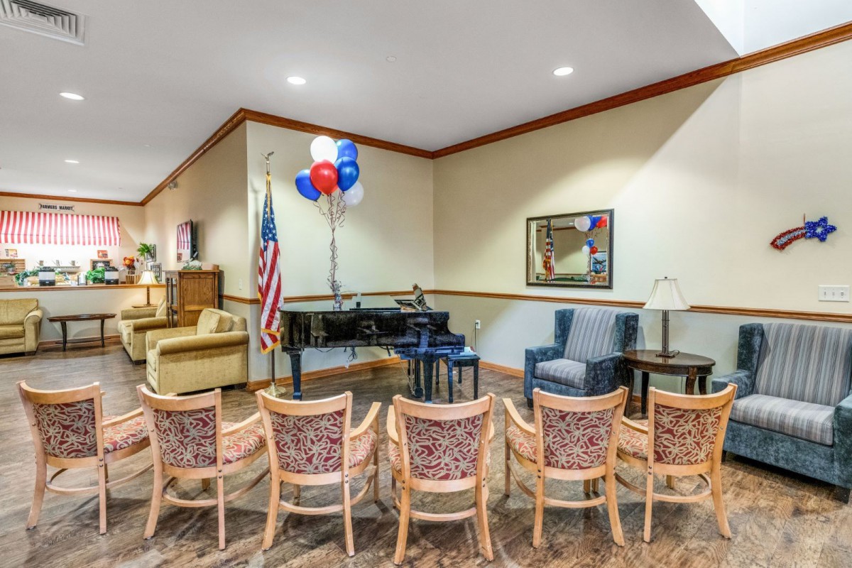 A hall setup with a piano, chairs, and festive balloons next to an American flag.