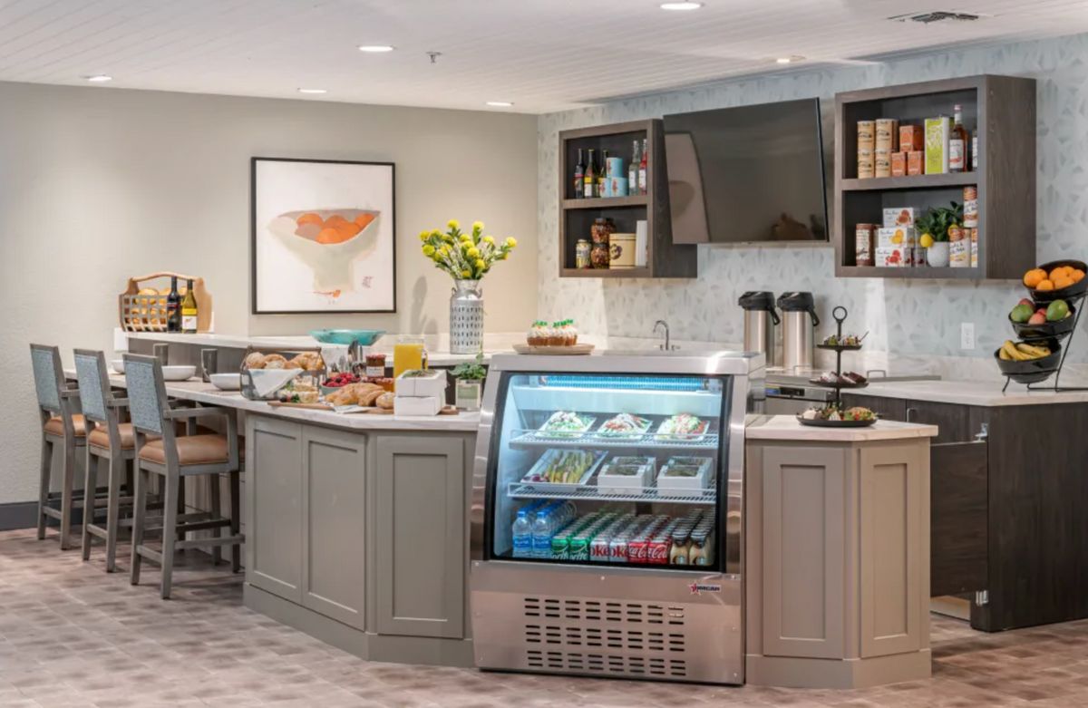 A cozy cafe interior featuring a counter with a beverage cooler, snacks, and a coffee station.