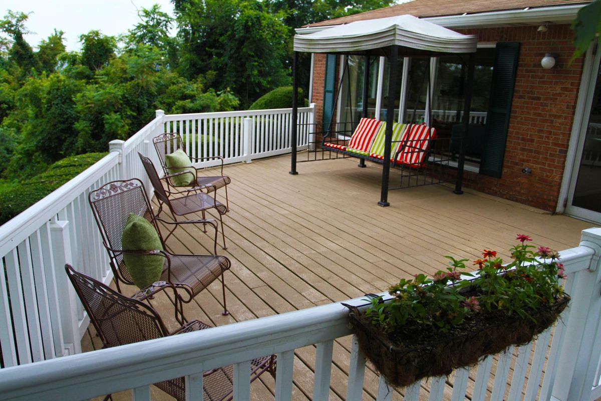 A spacious outdoor deck with seating and a canopy swing, surrounded by lush greenery.