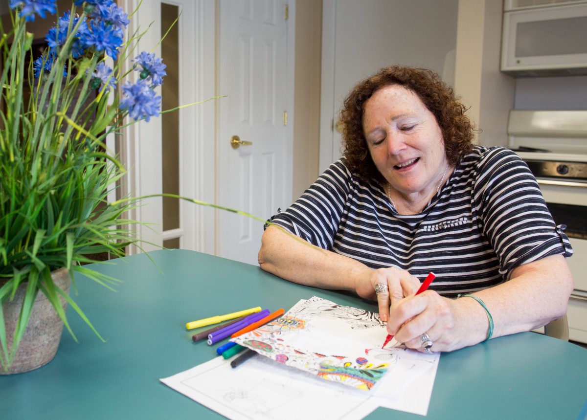 A woman is sitting at a table, engaged in drawing and coloring with various markers.