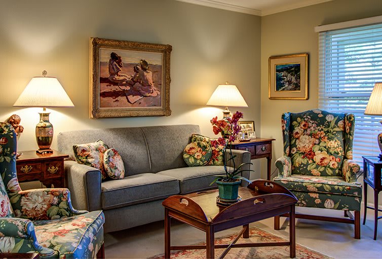 A cozy living room with a sofa and floral-patterned chairs, illuminated by warm lamps.