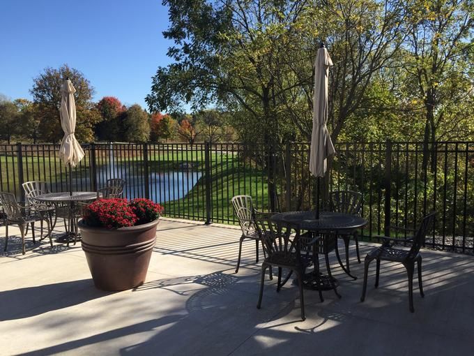 A serene patio setting with tables and chairs overlooking a pond and surrounded by trees on a sunny day.