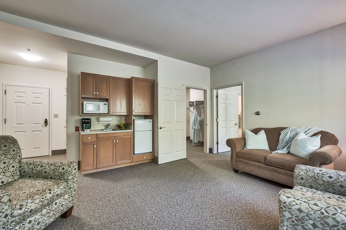 A cozy living room with a kitchenette, featuring a sofa and carpeted flooring.