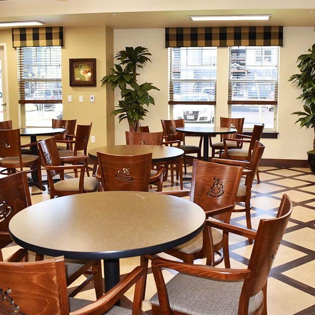 An empty dining area with round tables and wooden chairs in a well-lit room.