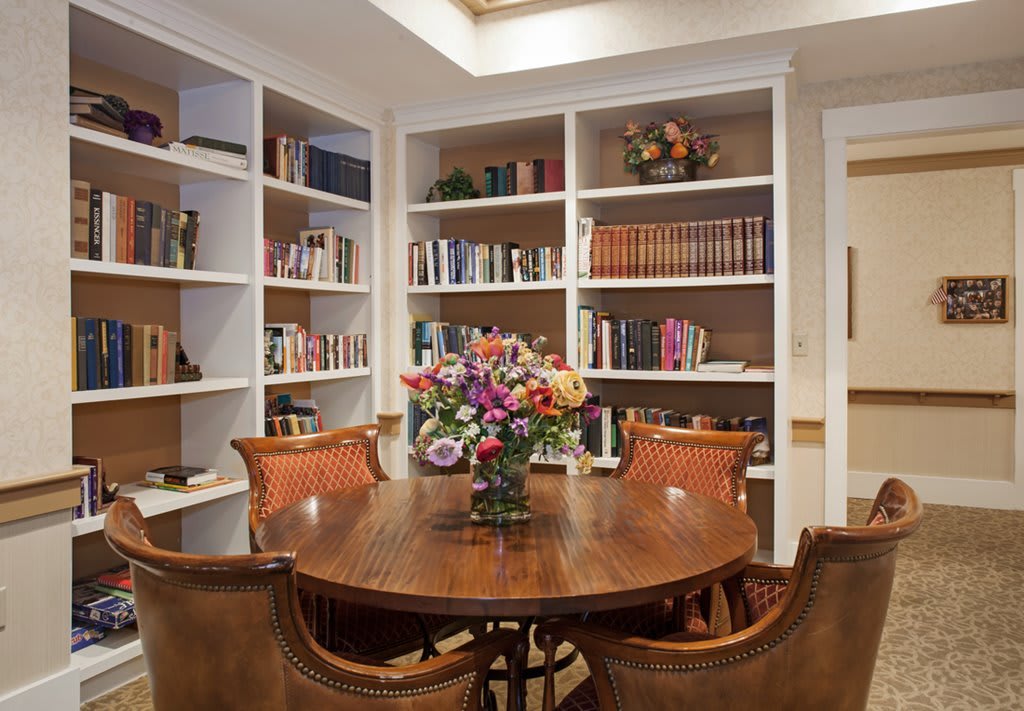 A cozy library room with bookshelves, a round wooden table, and a floral centerpiece.