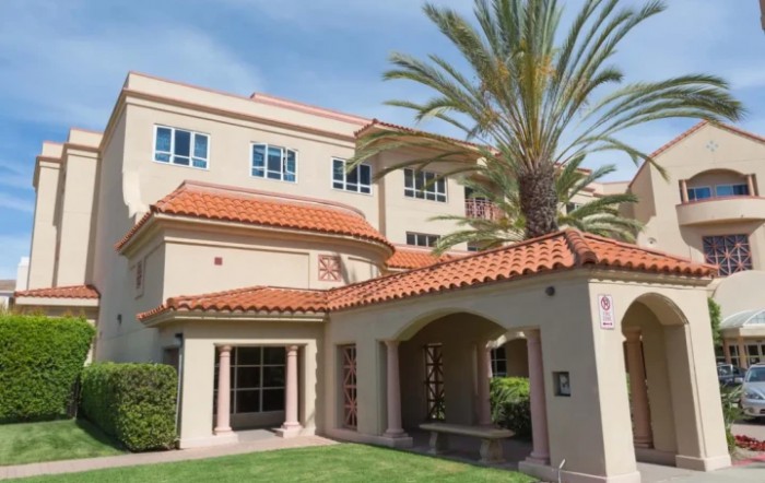 A Mediterranean-style building with a tiled roof, surrounded by palm trees and grass.