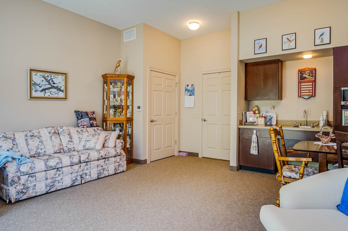 A cozy living room with a floral sofa, decorative cabinet, and carpeted floor.