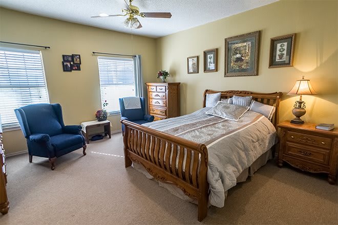 A cozy and well-decorated bedroom with a wooden bedframe, two blue armchairs, and a dresser near the window.