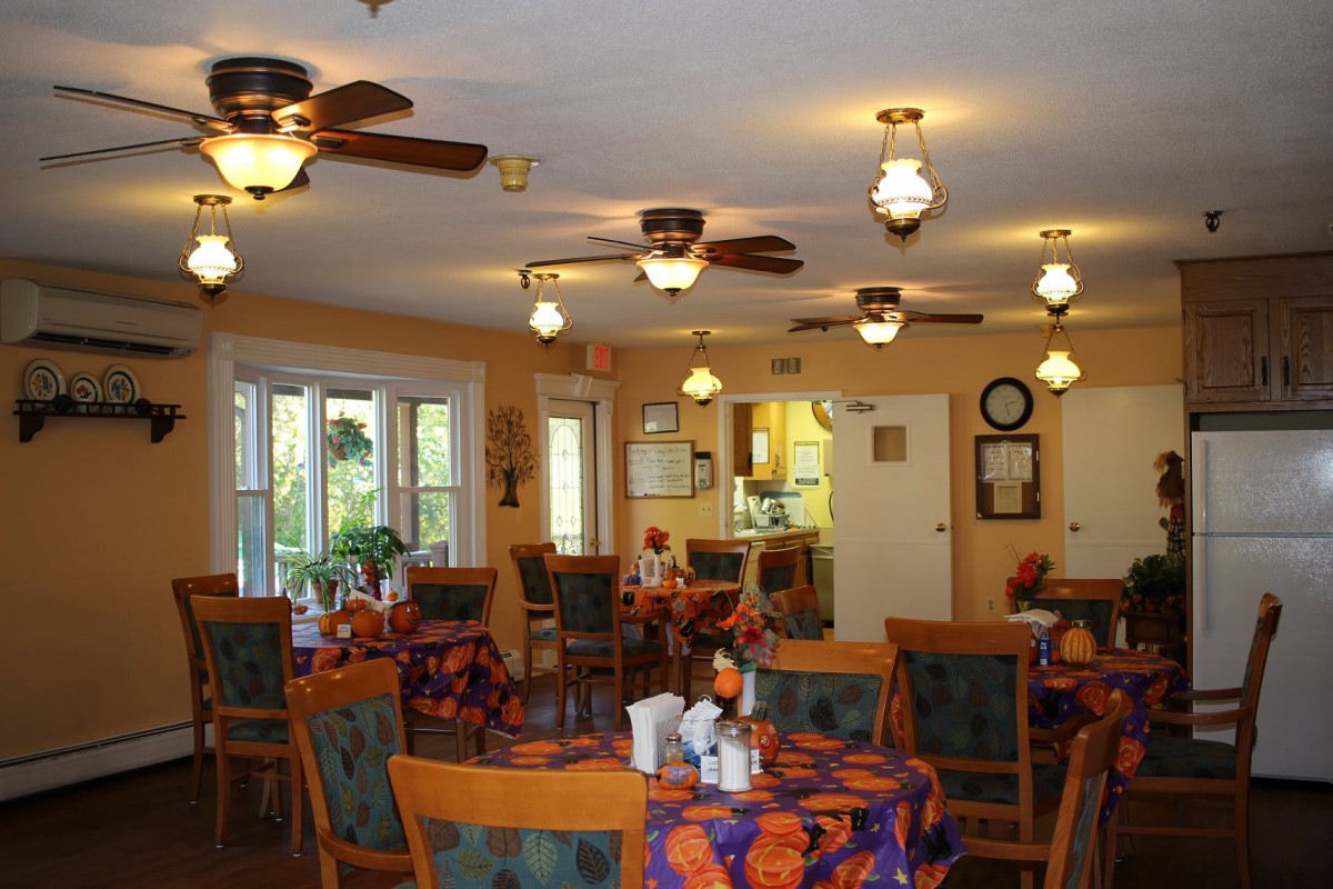 A cozy dining room with tables and chairs, featuring ceiling fans and warm lighting.