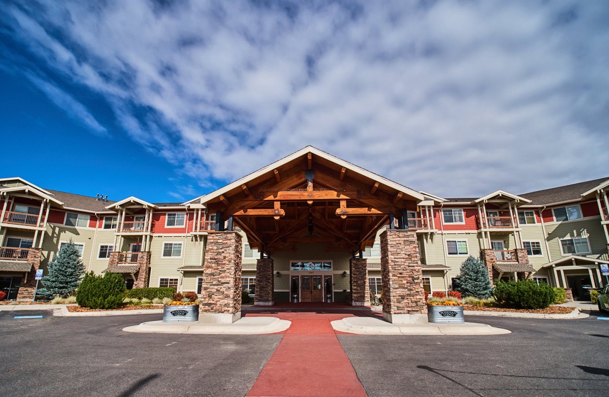 A welcoming entrance to a hotel with a wooden canopy and stone pillars under a partly cloudy sky.
