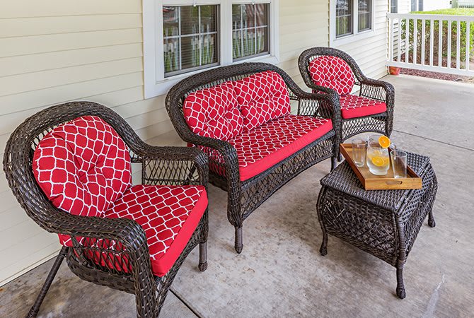 Outdoor wicker patio set with red-patterned cushions, featuring a loveseat, two chairs, and a table.