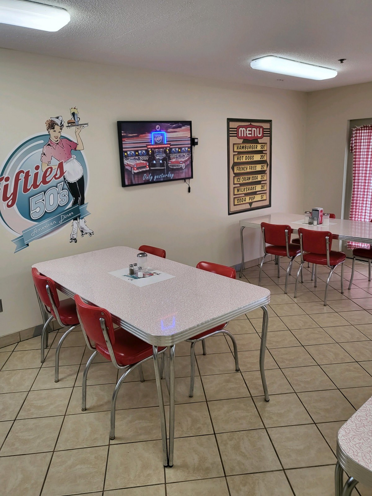 A retro-themed diner interior with red chairs, white tables, and classic wall art.