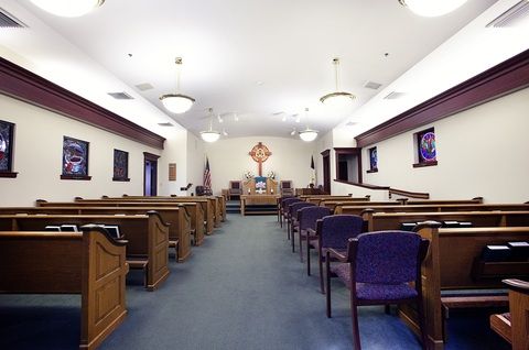 Interior view of a church with wooden pews and a cross at the altar.