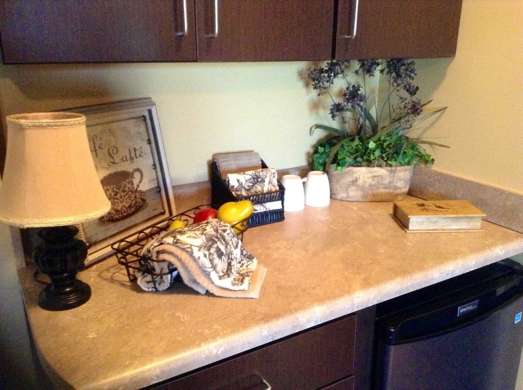 A kitchen counter with decorative items, including a lamp, framed artwork, and a flower arrangement.