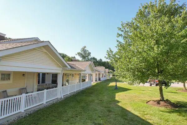A row of houses with porches under a clear blue sky, surrounded by trees and grassy areas.