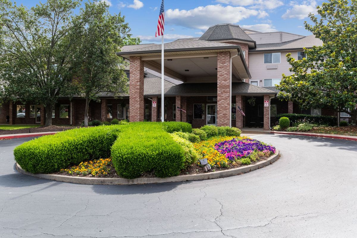 A well-maintained building entrance with vibrant flower beds and an American flag.
