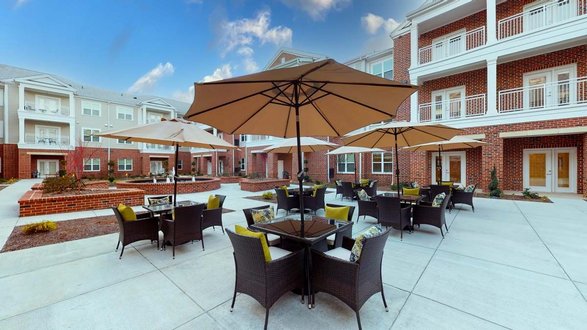 A sunny outdoor patio with tables, chairs, and umbrellas in front of a brick building.