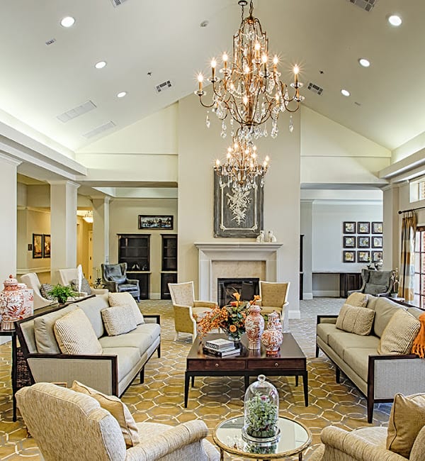 A luxurious living room with a central chandelier, elegant sofas, and a decorative fireplace.