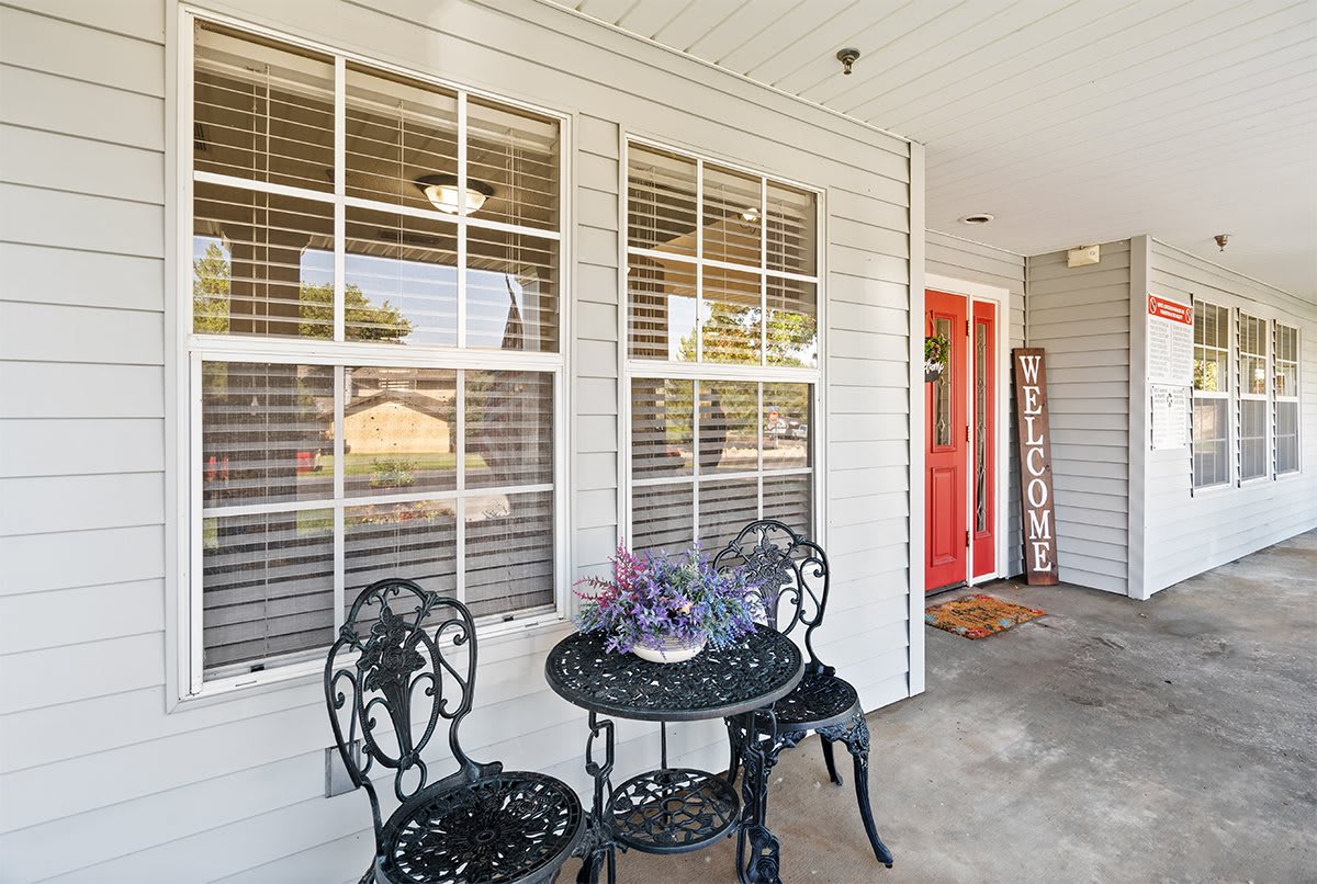 A cozy front porch with a small metal table and chairs, potted plant, and a red front door.