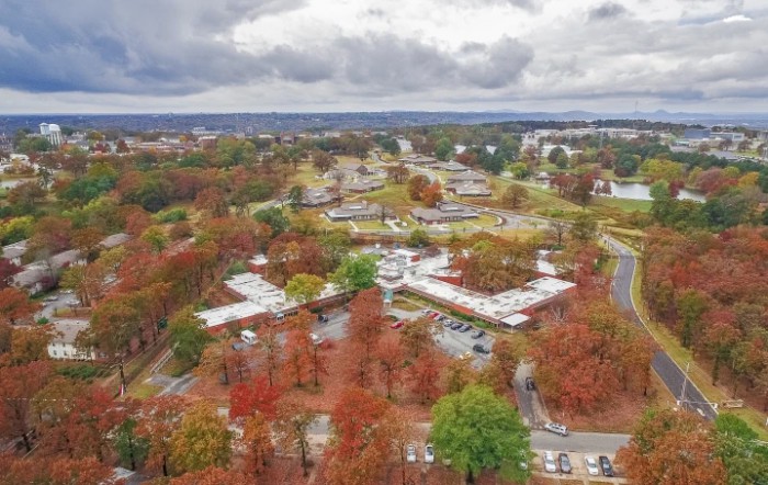 Aerial view of a landscape with buildings surrounded by trees in autumn colors under a cloudy sky.
