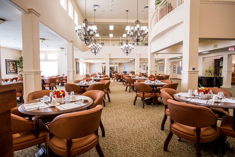 An elegant dining area with neatly arranged tables and chairs under grand chandeliers.